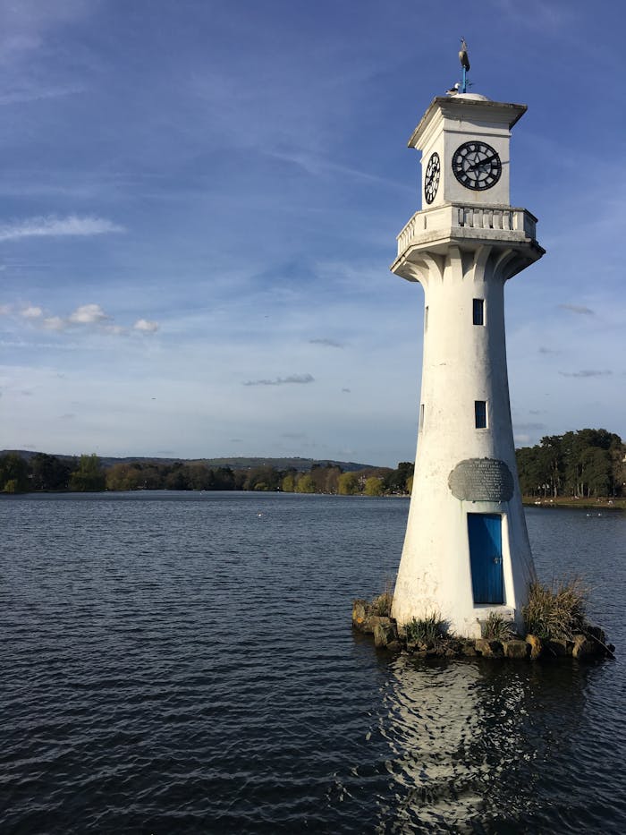 A tranquil scene of Scott Memorial Lighthouse at Roath Park Lake, Cardiff, under a clear sky.